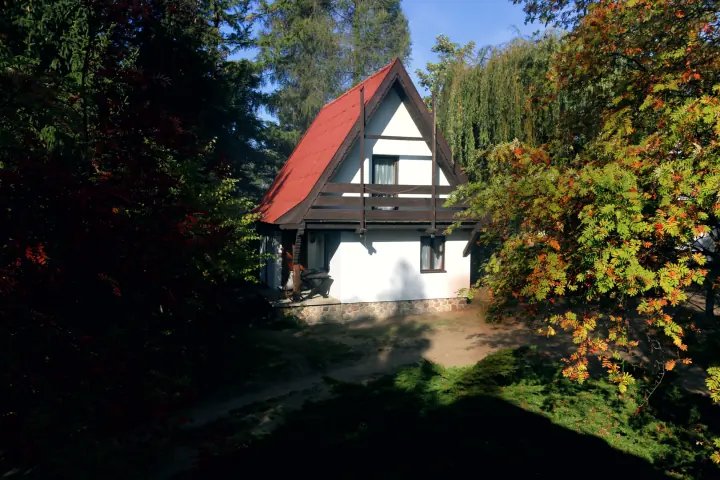 Domek piętrowy z czerwonym dachem wśród jesiennych drzew
