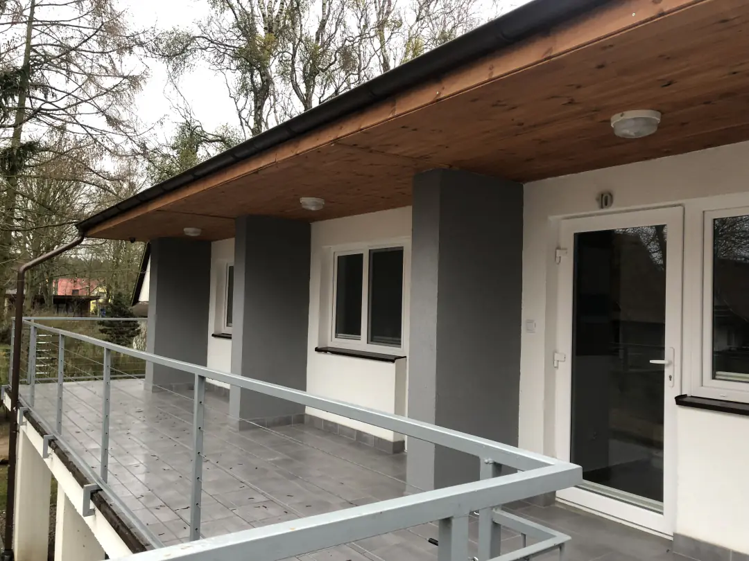 Pawilon z pokojami: zadaszony taras z balustradą przed wejściami do pokoi