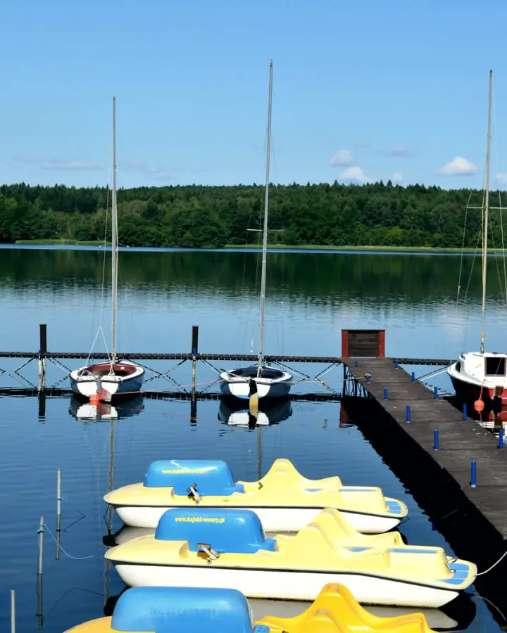 Pomost z żółto-niebieskimi rowerami wodnymi i jachtami
