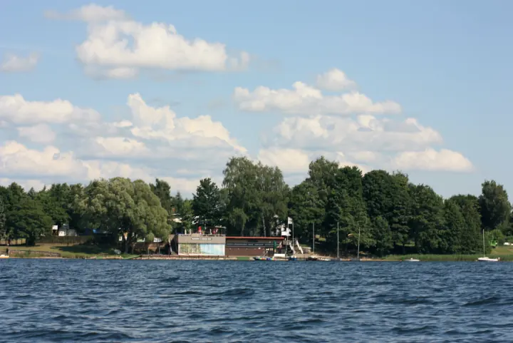 Ośrodek Rejs widziany z&nbsp;Jeziora Charzykowskiego: budynek przystani wśród drzew, łodzie przy brzegu