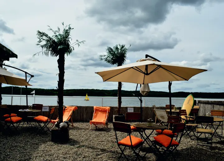 Pomarańczowe leżaki, palmy i&nbsp;parasole na tarasie Beach Baru nad Jeziorem Charzykowskim