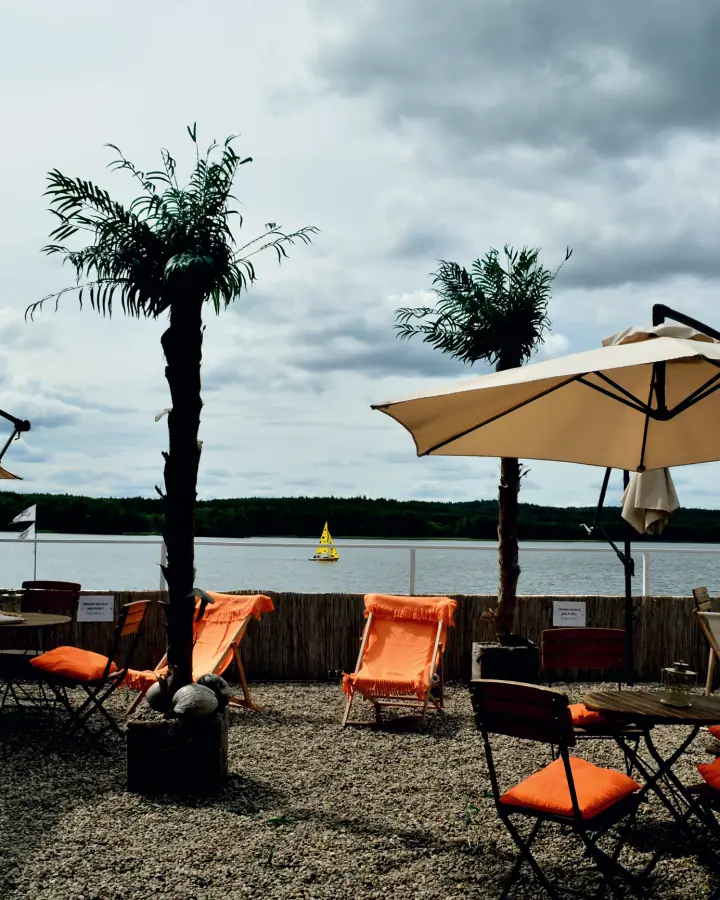 Pomarańczowe leżaki, palmy i parasole na tarasie Beach Baru nad jeziorem