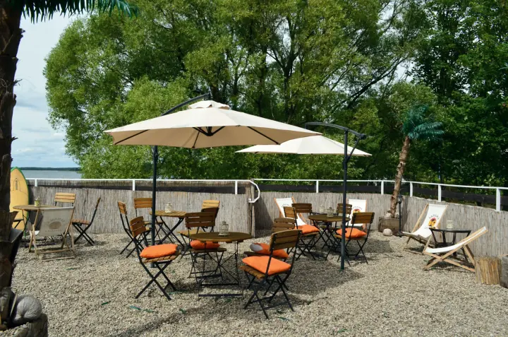Taras Beach Baru nad jeziorem: parasole, pomarańczowe krzesła i leżaki wśród drzew