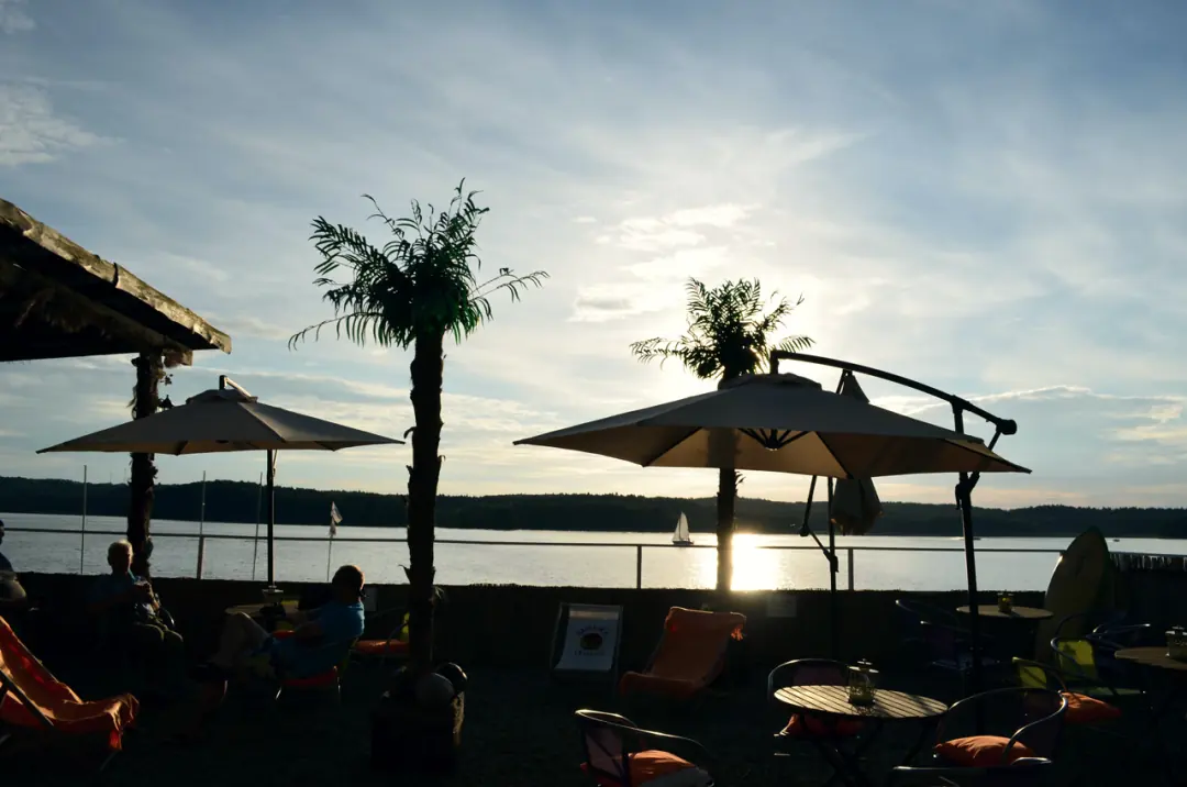 Zachód słońca nad jeziorem, sylwetki palm i&nbsp;parasoli Beach Baru
